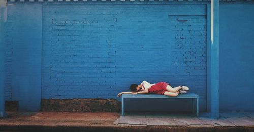 Young woman sleeping on bench by wall