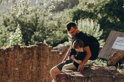 Woman sitting on rock against trees