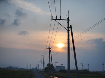 Low angle view of electricity pylon on field against sky during sunset