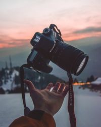 Close-up of hand holding camera against sky during sunset