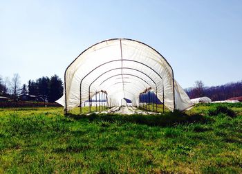 Greenhouse on grassy field against clear sky