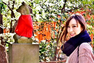 Portrait of smiling young woman standing against tree