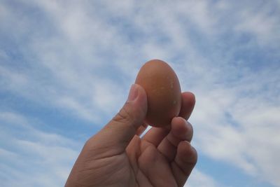 Close-up of hand holding egg against sky
