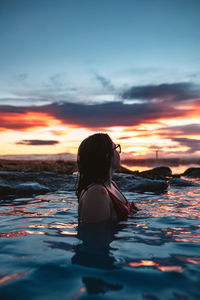 Rear view of woman swimming in sea during sunset