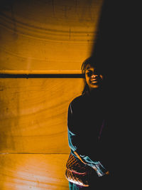 Happy young woman standing against wooden wall in darkroom