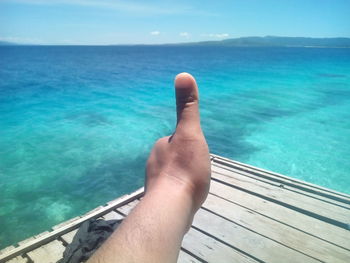 Cropped hand of man gesturing thumbs up sign against sea