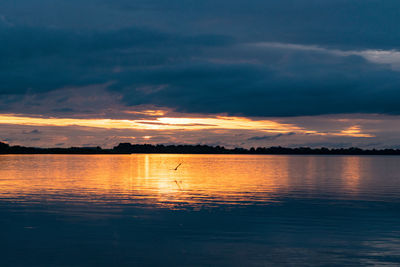 Scenic view of lake against cloudy sky during sunset