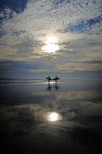 Silhouette people on beach against sky during sunset