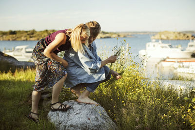 Young friends by flowers at harbor against sky