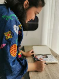 Portrait of a young girl wearing blue outfit writing at a book on the table 