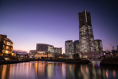 Illuminated buildings by river against sky in city