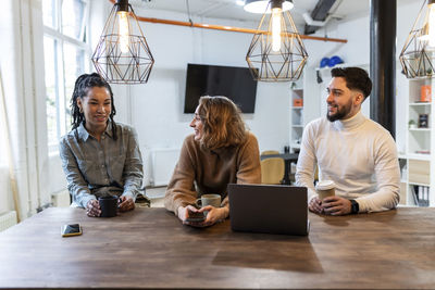 Happy coworkers sitting together having coffee in cafeteria