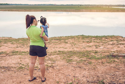 Rear view of woman with daughter standing at riverbank