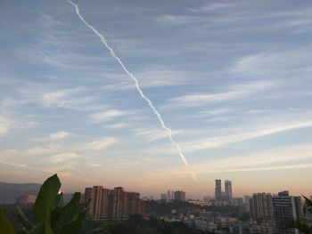 Low angle view of vapor trail over cityscape against sky
