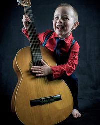 Full length of cute boy standing with guitar against black background