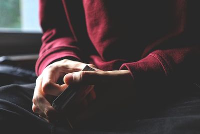 Midsection of person holding cards while sitting by window at home