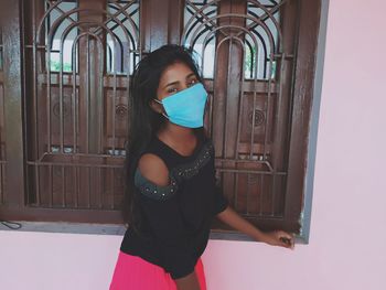 Portrait of woman standing against door wearing surgical mask 