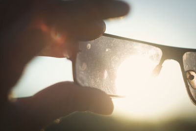 Close-up of hand holding camera against sky