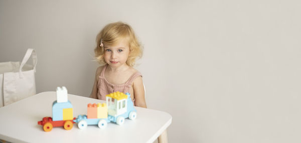 Pretty caucasian 1,2 year old with blond curly hair playing with colourful construction, toy train