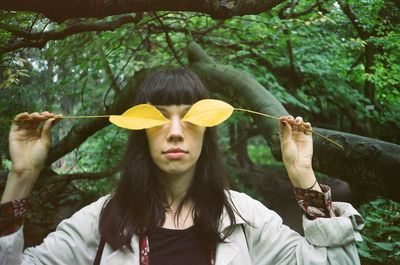 Young woman holding yellow leaves against trees at park