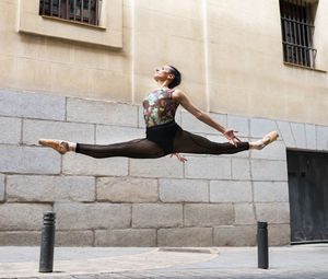 Dancer wearing leotard dancing while jumping with legs stretched on footpath