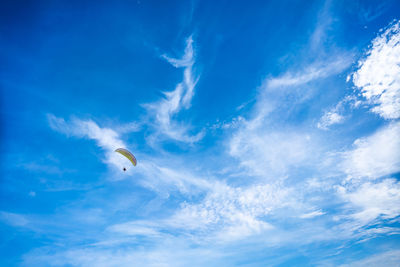 Low angle view of person paragliding against blue sky