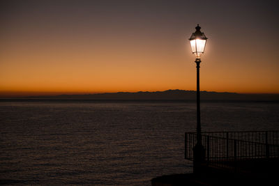 Street light by sea against sky during sunset