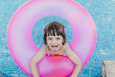 Portrait of smiling girl sticking out tongue on inflatable ring in swimming pool