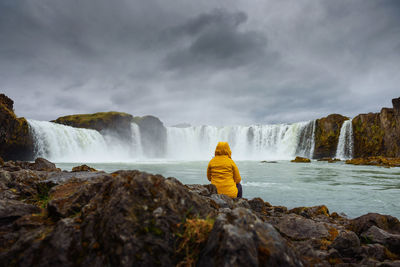 Rear view of man looking at waterfall against sky