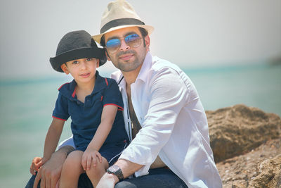 Portrait of father and son sitting on rock at beach