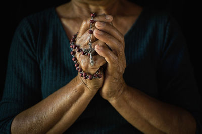 Midsection of woman praying with rosary