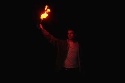 Young man holding flaming torch while standing at night