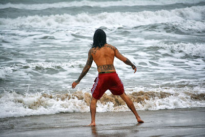 Rear view of shirtless man wading in sea