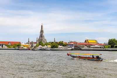 A long-tailed boat is sailing on the chao phraya river and also get to see the wat arun riverside. 