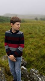 Boy wearing sweater looking away while standing on field