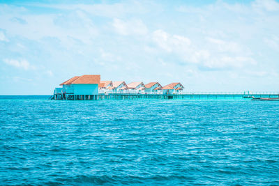 Stilt house by sea against sky