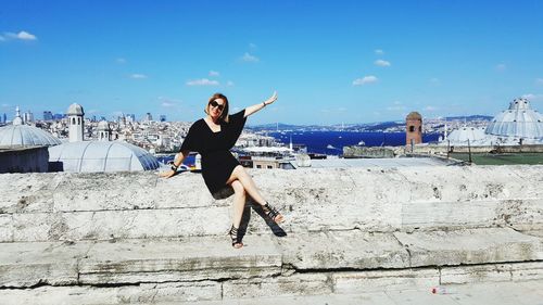 Portrait of smiling woman with arms raised sitting on concrete wall