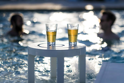 Beer glasses on table against swimming pool