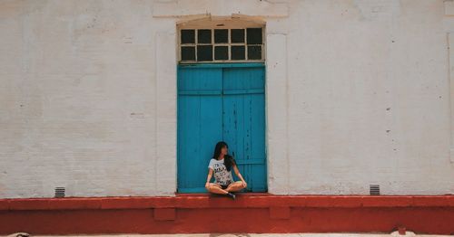 Woman sitting against window of building