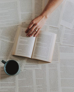 High angle view of hand over book by coffee cup on table