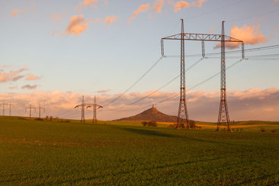 Electricity pylon on field against sky during sunset