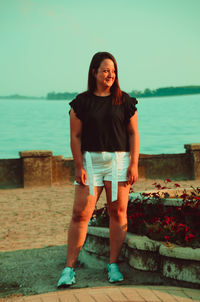 Portrait of a smiling young woman standing against sea