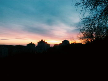 Silhouette of buildings against cloudy sky at sunset