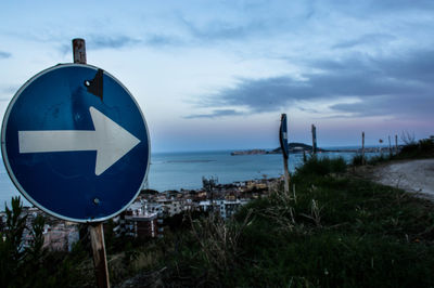 Close-up of road sign by sea against sky