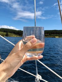 Midsection of person holding sailboat in sea against sky