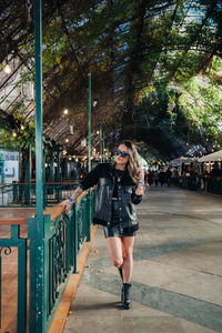 Full length portrait of young woman standing by tree in city