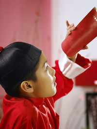 Close-up of teenage boy in traditional clothes looking through paper