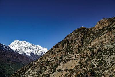 Low angle view of snowcapped mountains against clear blue sky