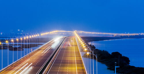 Light trails on bridge against sky at night