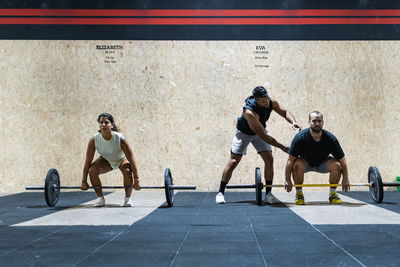 Full body group of strong hispanic athletes lifting heavy barbells near wall in light gym during weightlifting training together